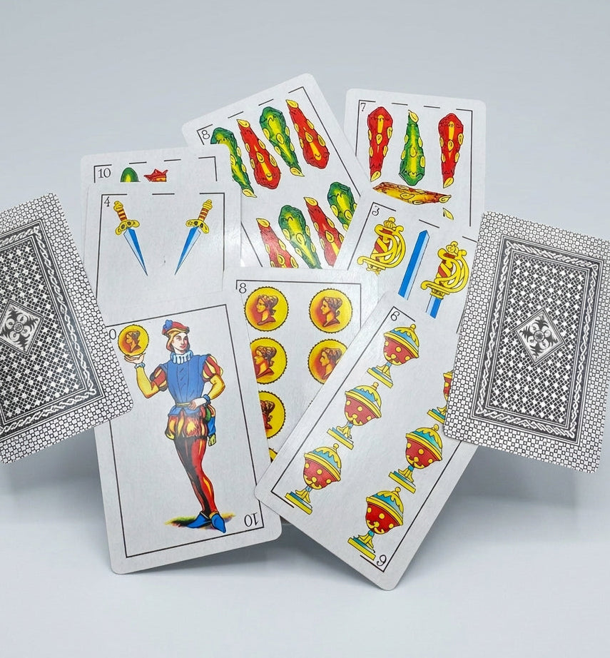 Baraja Española playing cards displaying traditional coins, cups, swords and clubs suits, a court card and black patterned card backs.