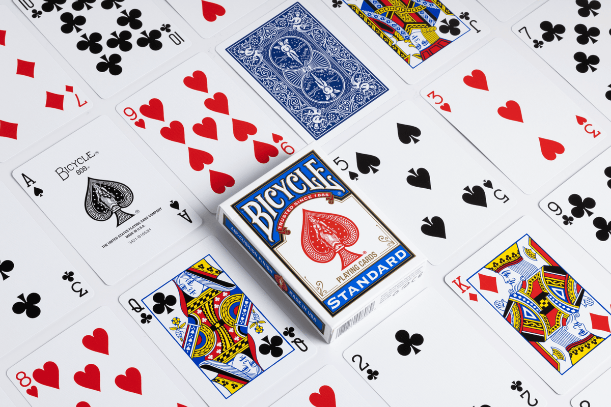 Bicycle Standard blue tuck box surrounded by playing cards showing classic court cards, number cards, the ace of spades and a blue card back.