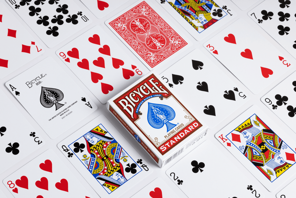Bicycle Standard red tuck box surrounded by playing cards showing classic court cards, number cards, the ace of spades and a red card back.