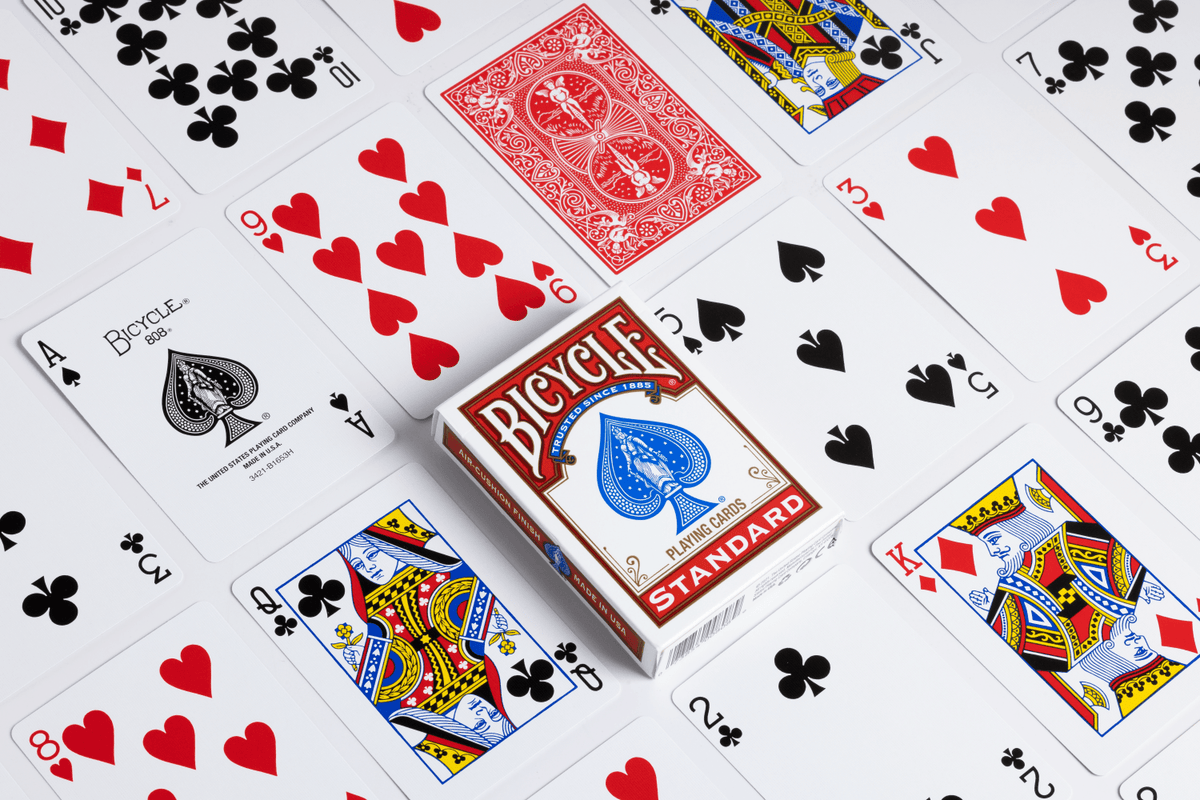 Bicycle Standard red tuck box surrounded by playing cards showing classic court cards, number cards, the ace of spades and a red card back.