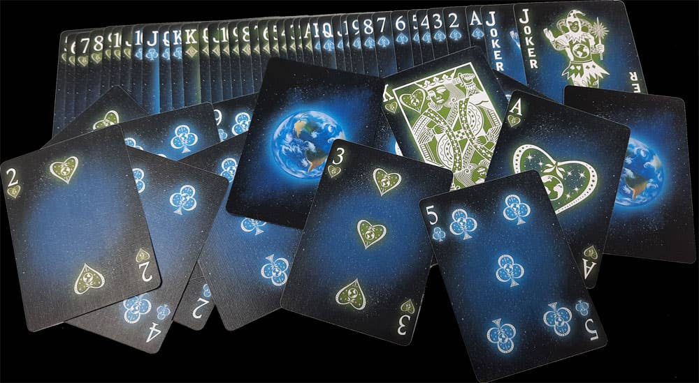 Bicycle Starlight Earth Glow cards spread on a black background, showing custom blue and green pips, court cards, Jokers and Earth-themed backs.