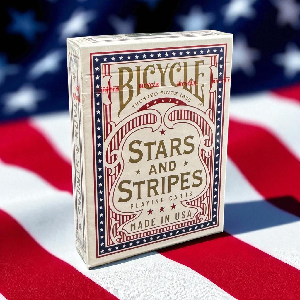 Bicycle Stars and Stripes Playing Cards sealed deck featuring patriotic red, white and blue artwork, photographed against an American flag background.