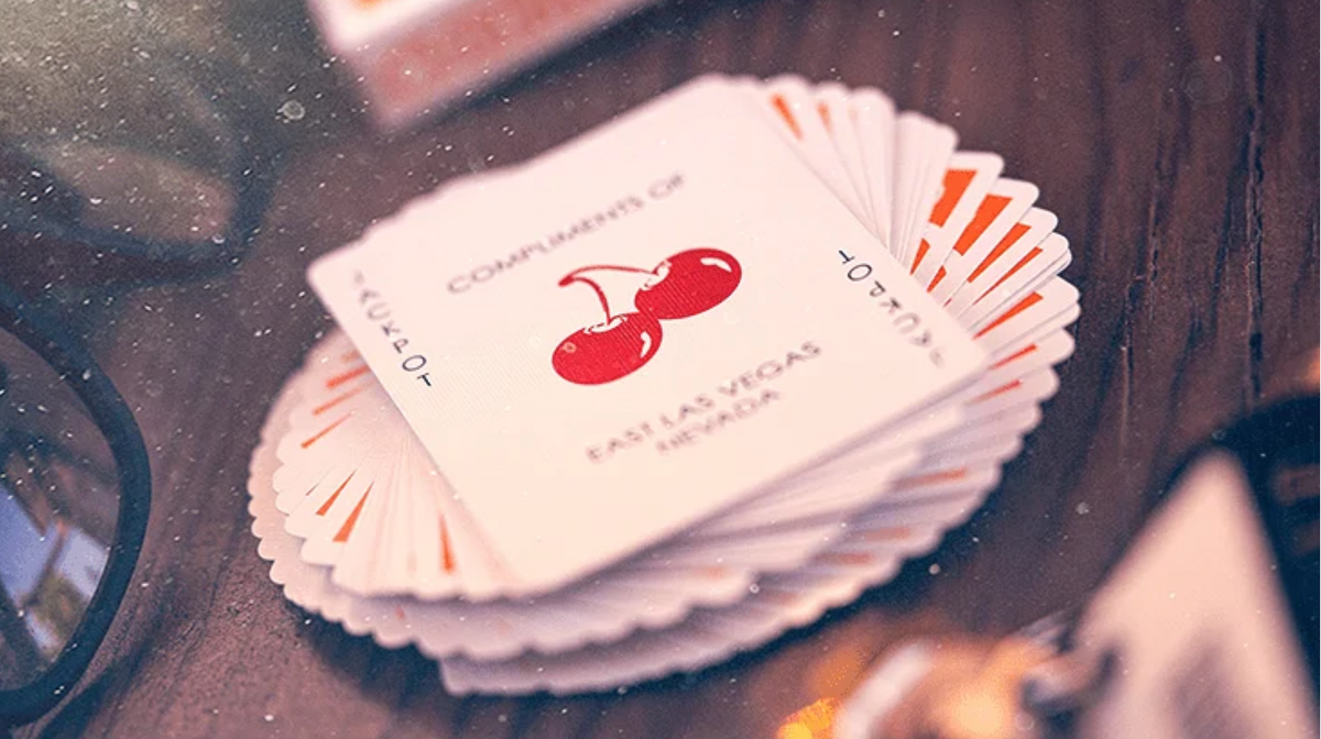 Custom Joker card from Cherry Casino Summerlin Sunset Orange Playing Cards featuring red cherry artwork and East Las Vegas lettering, displayed on a fan of orange playing cards.