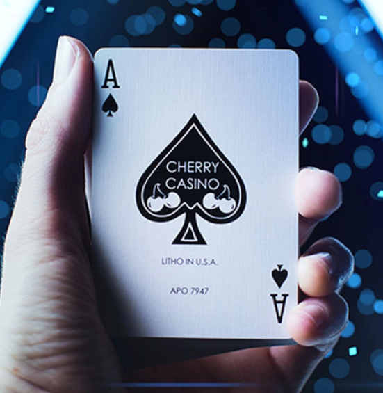 Close-up of the custom Ace of Spades from Cherry Casino Tahoe Blue Playing Cards, held in a hand against a blue illuminated background, featuring the distinctive black Cherry Casino spade emblem and cherry artwork.