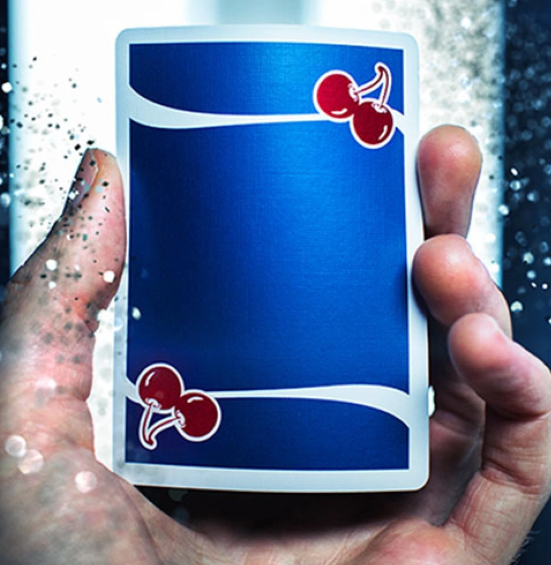 Close-up of a Cherry Casino Tahoe Blue playing card held in a hand, showing the vibrant blue card back with red cherry artwork, flowing white stripes and white border.