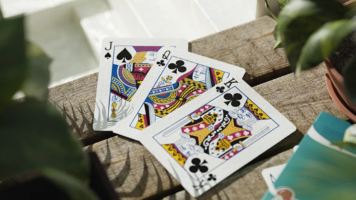 Cherry Casino Tropicana Teal Playing Cards featuring the Jack of Spades, Queen of Clubs and King of Clubs, displayed on a rustic wooden table alongside the teal card backs.
