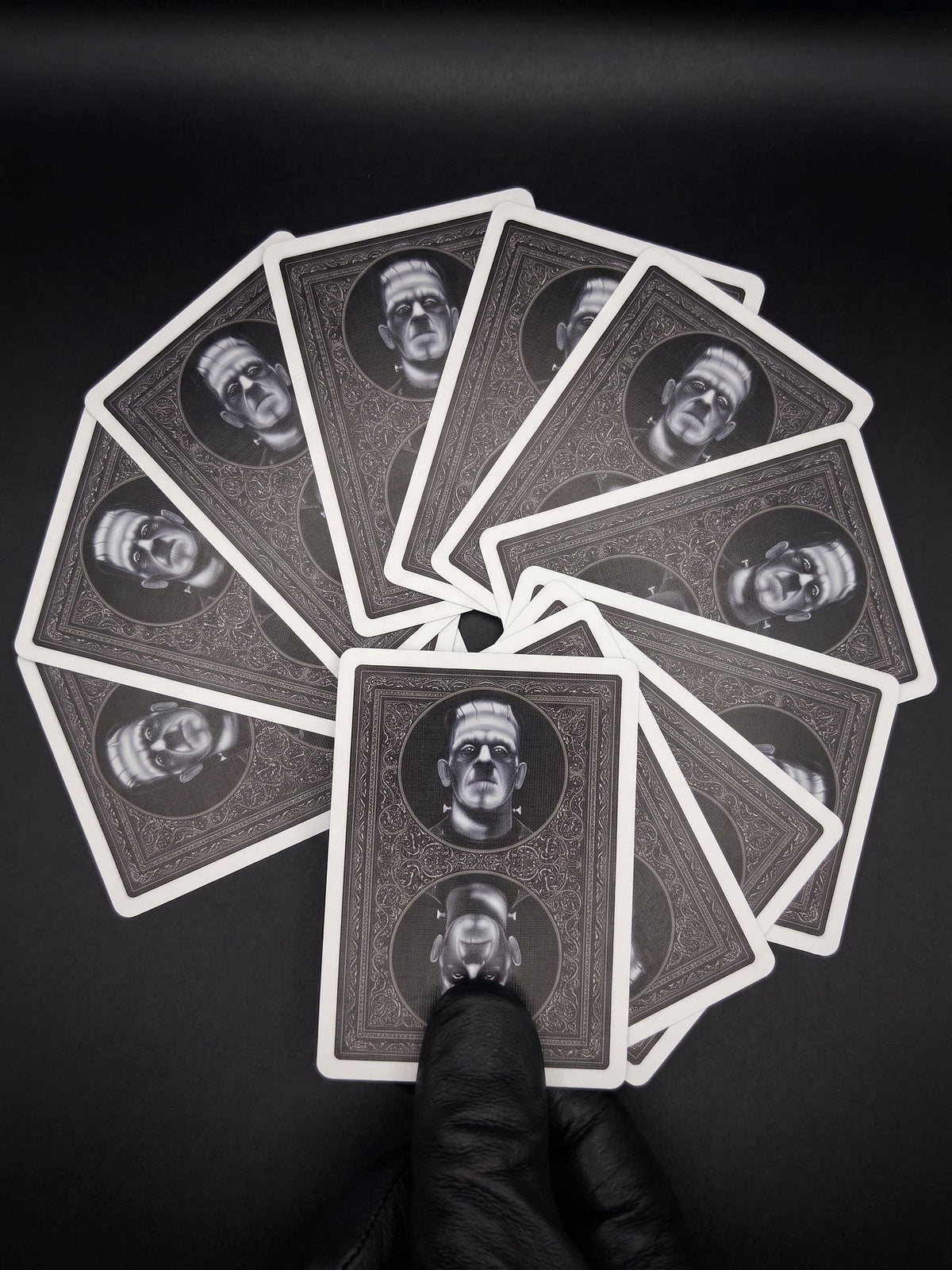 Classic Monsters Playing Cards by Collectible Playing Cards showing black and white Frankenstein card backs with ornate gothic borders, fanned out against a dark background.