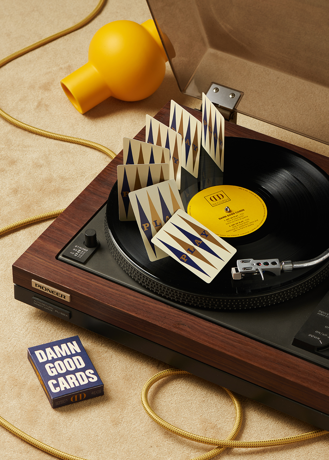 Damn Good Cards No. 7 by Dan & Dave showing blue and gold PLAY card backs arranged across a vinyl record on a vintage turntable, with the blue tuck box alongside.