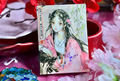 Four Beauties Spring Playing Cards featuring an illustrated Chinese woman in a pink traditional dress, photographed with cherry blossoms, a red teacup and oriental accessories.
