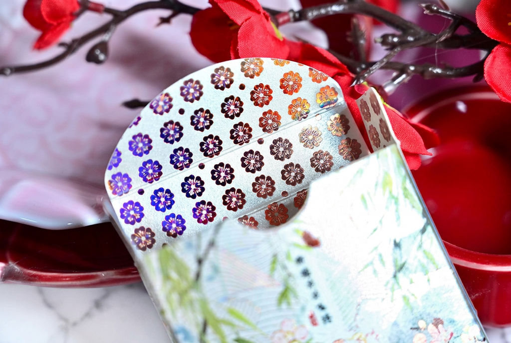 Four Beauties Spring Playing Cards showing the opened tuck box with colourful metallic floral patterns inside, decorative bamboo artwork on the packaging and red cherry blossoms in the background.