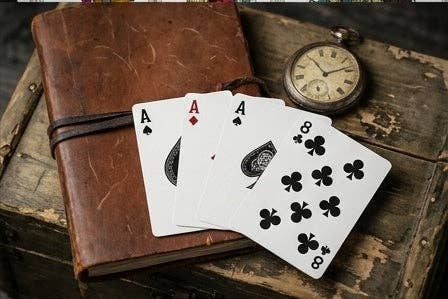 Haunted Dolls Playing Cards by CPC showing three custom Aces and the Eight of Clubs arranged on a vintage leather journal beside an antique pocket watch.