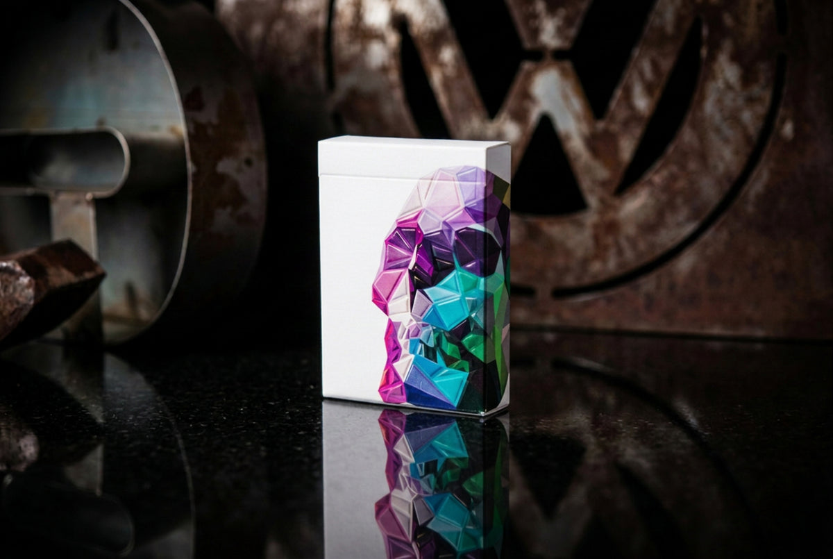 Memento Mori Playing Cards by Chris Ramsay – Original geometric skull deck displayed on a reflective metal surface with an industrial background.