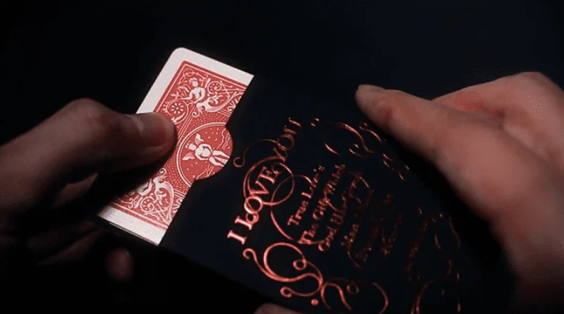 Love Promise of Vow Red Playing Cards by BOCOPO being removed from the black and red decorative tuck box, showing the red card back design.