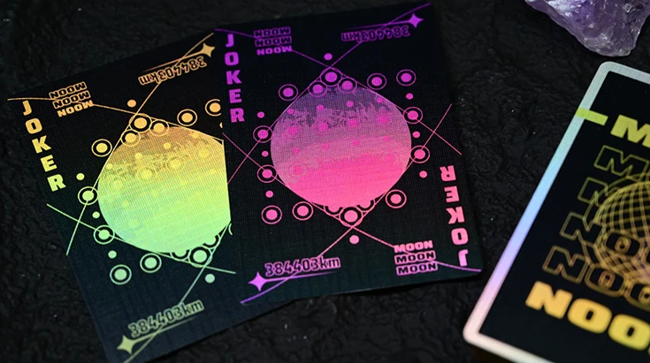 Moon Black Holo Playing Cards by Hiddenlight showing two custom Joker cards with black backgrounds, holographic green, yellow and pink lunar artwork, geometric patterns and colourful moon designs.