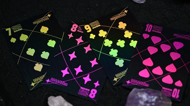 Moon Black Holo Playing Cards by Hiddenlight showing custom 7, 8, 9 and 10 cards with black backgrounds, vibrant holographic pink, green and yellow suit symbols and geometric lunar-inspired artwork.