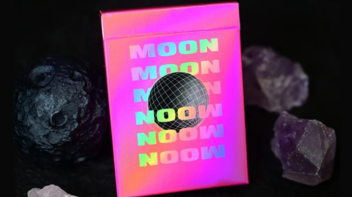 Moon Noon Holo Pink Playing Cards featuring a vibrant holographic pink tuck box with rainbow lettering and black wireframe disco ball artwork, displayed alongside moon rocks and purple crystals.
