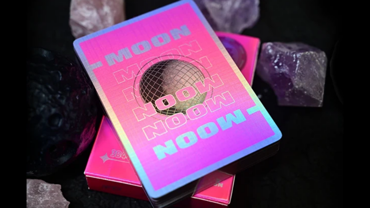 Moon Noon Holo Pink Playing Cards showing the holographic card back design with rainbow foil borders, pink gradient artwork, MOON NOON lettering and a central black wireframe disco ball, displayed with the matching tuck box.
