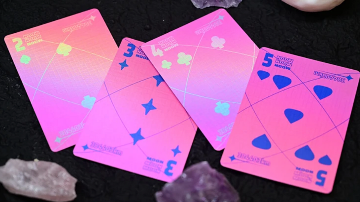 Moon Noon Holo Pink Playing Cards showing four custom numbered cards with vibrant pink backgrounds, holographic rainbow details, blue suit symbols and geometric lunar-inspired artwork.