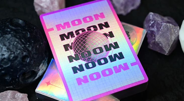 Moon White Holo Playing Cards by Hiddenlight showing the custom card back with iridescent rainbow holographic artwork, bold MOON lettering, a central black wireframe sphere and vibrant pink borders.