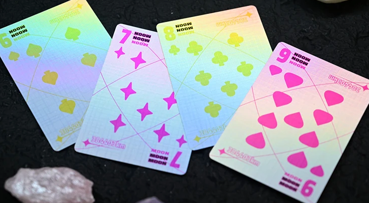 Moon White Holo Playing Cards by Hiddenlight showing custom 6, 7, 8 and 9 number cards with iridescent rainbow holographic backgrounds, colourful pink, green and yellow suit symbols and geometric lunar-inspired artwork.