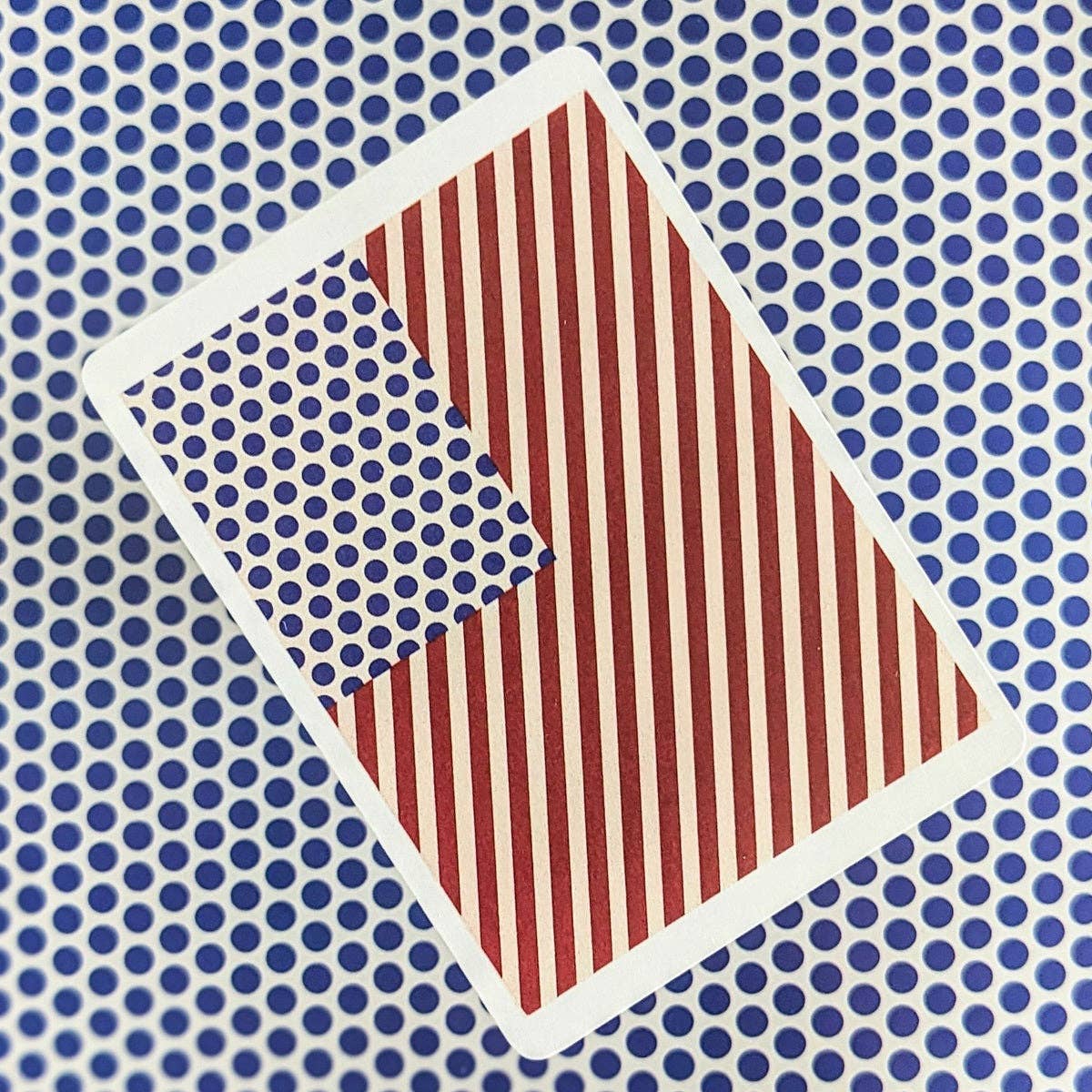Reverse of a Piatnik Roy Lichtenstein playing card featuring a stylised American flag with red stripes and blue dots, displayed on a blue polka-dot background.