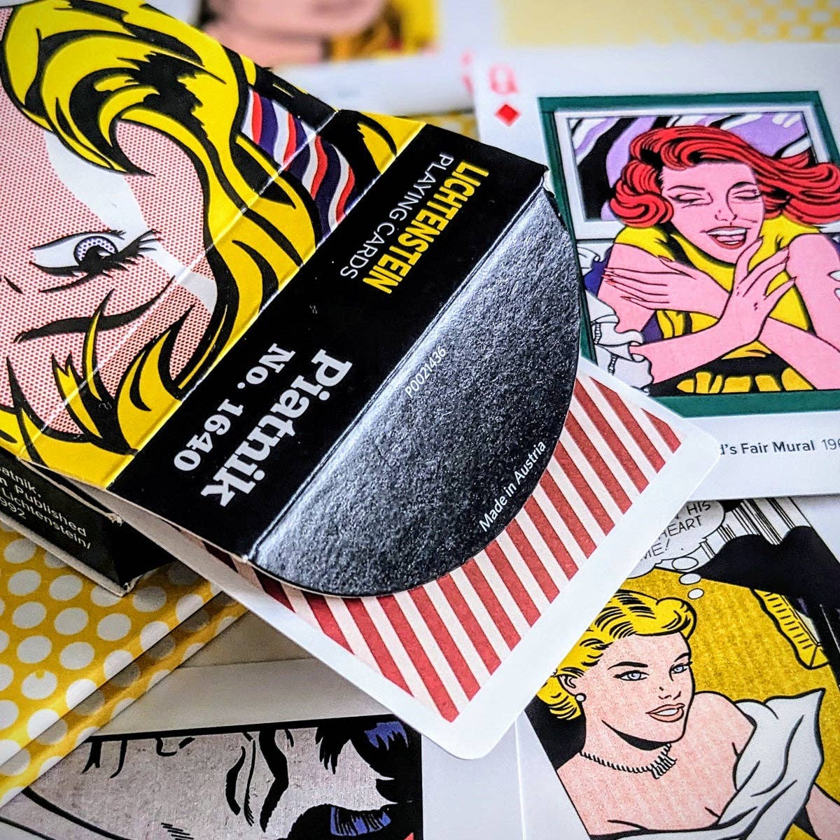 Piatnik Roy Lichtenstein Playing Cards showing the illustrated tuck box, Queen of Diamonds, colourful comic-style artwork and red-striped card back.