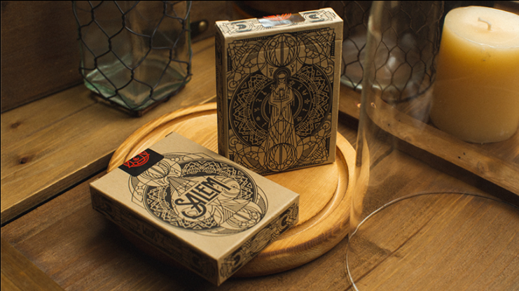 Salem Playing Cards tuck boxes displayed on a wooden tray beside a candle, showing the kraft-coloured packaging with intricate black ornamental artwork