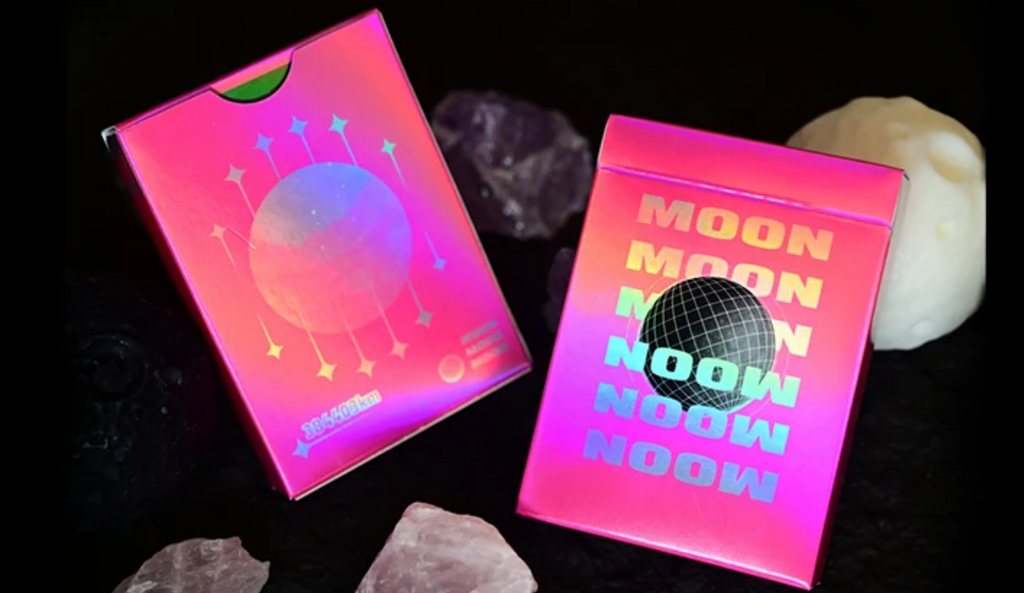 Moon Noon Holo Pink Playing Cards showing the front and back of the vibrant neon pink tuck box, featuring holographic rainbow lettering, a black wireframe disco ball and colourful lunar artwork.